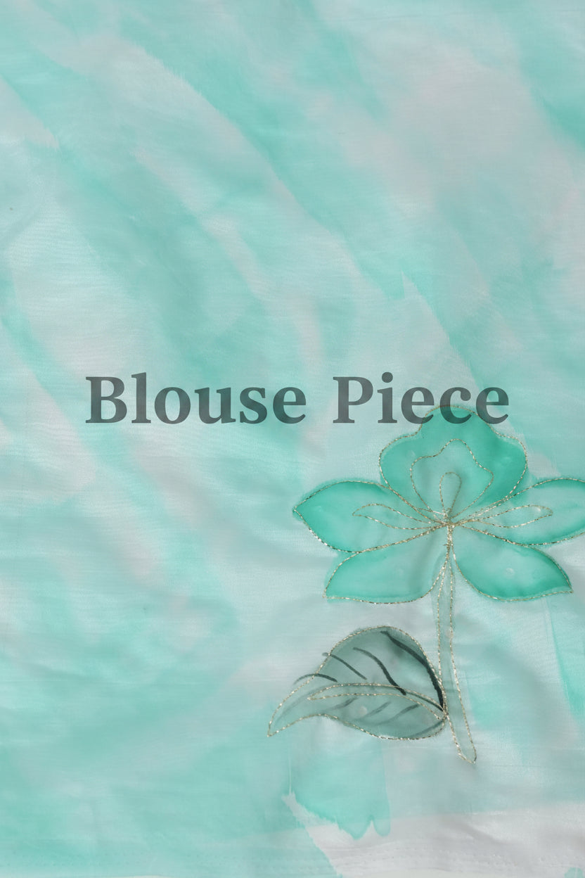 A close-up of a light aqua and white marbled fabric with a small embroidered or appliqué flower motif in matching aqua tones. The text 'Blouse Piece' is overlaid across the center.